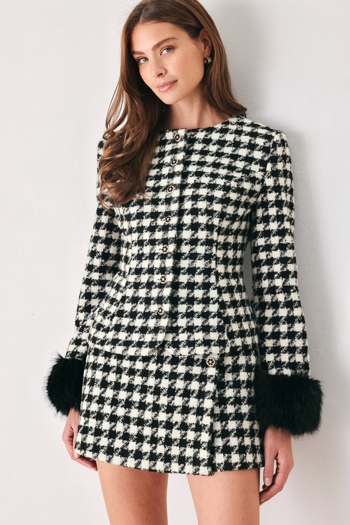 Woman wearing a black and white long sleeve houndstooth tailored jacket with front button closure and faux fur trim around the wrists | FREEMARKET