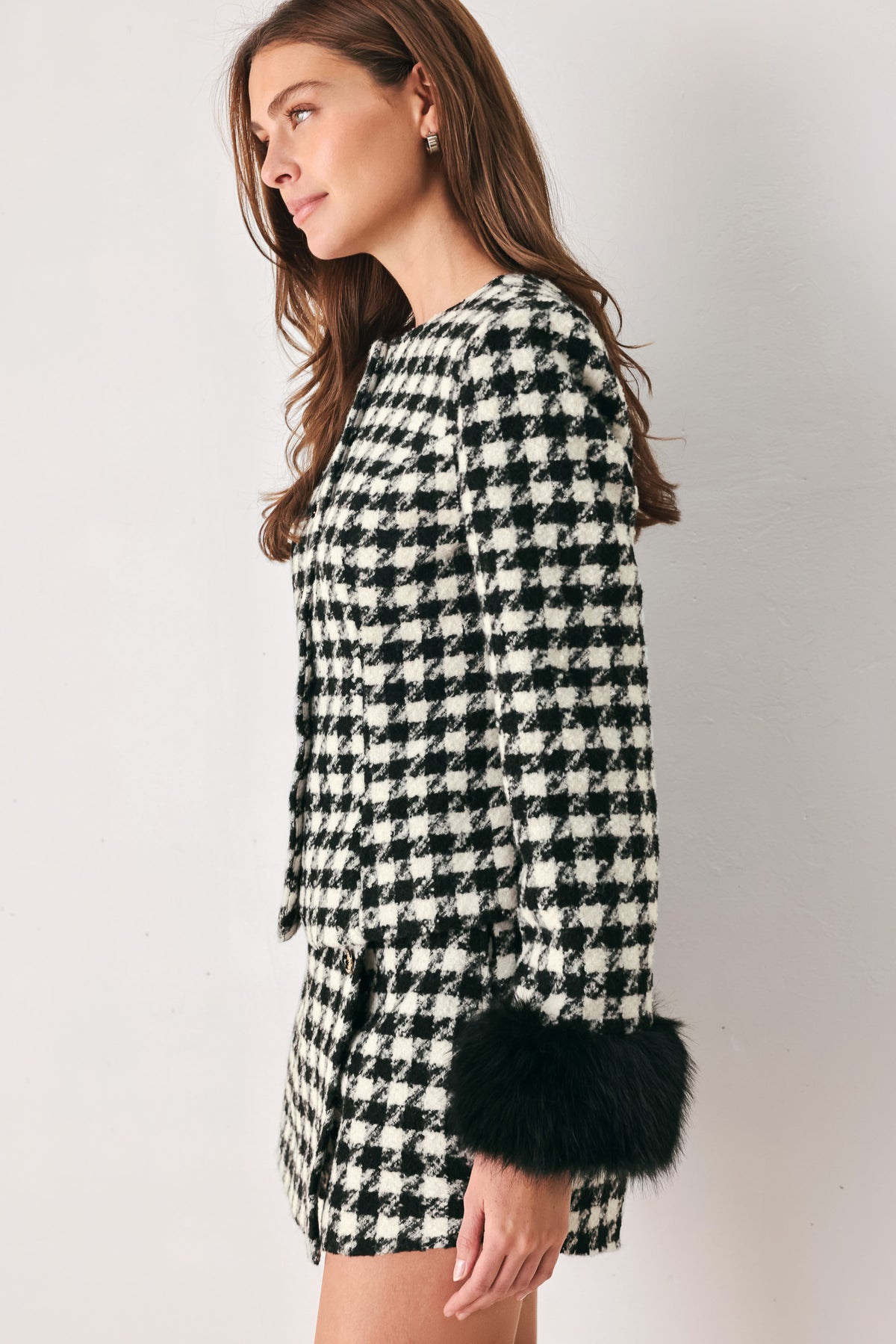 Woman wearing a black and white long sleeve houndstooth tailored jacket with front button closure and faux fur trim around the wrists | FREEMARKET