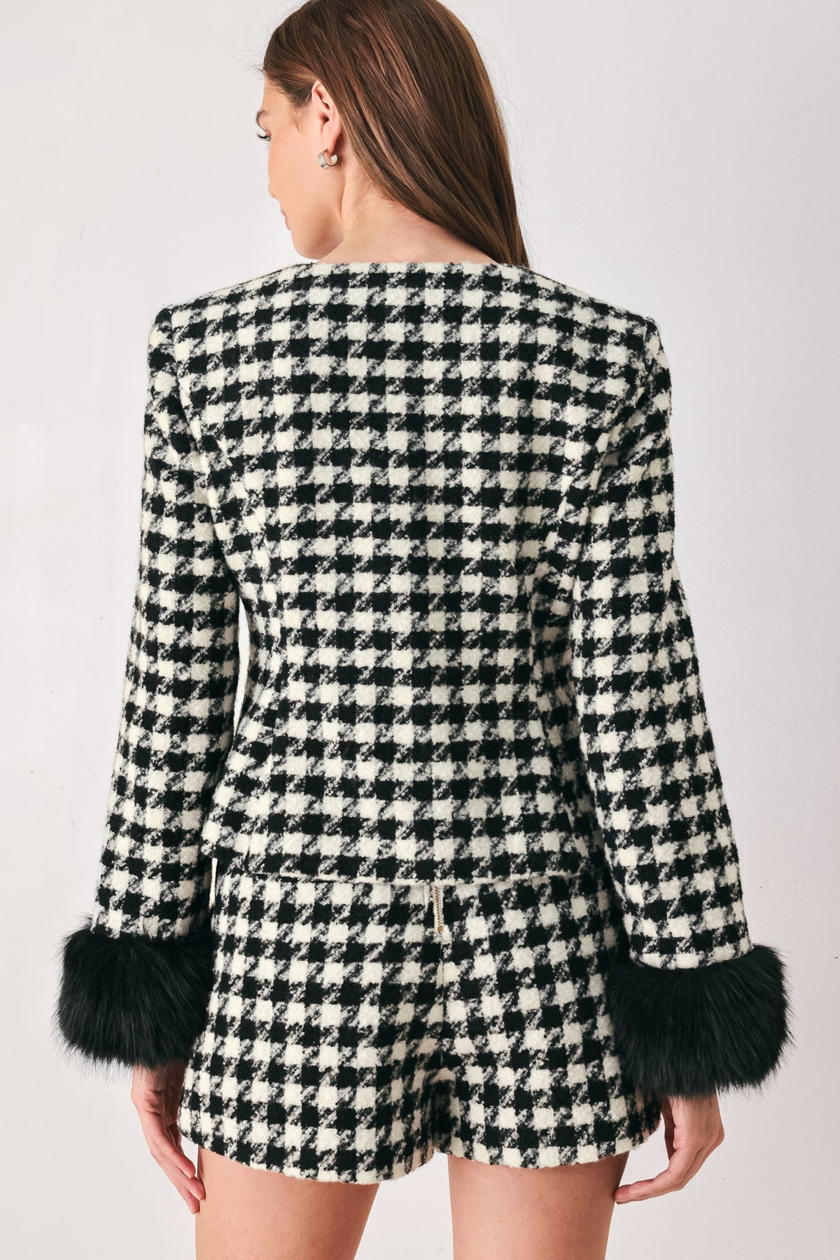 Woman wearing a black and white long sleeve houndstooth tailored jacket with front button closure and faux fur trim around the wrists | FREEMARKET