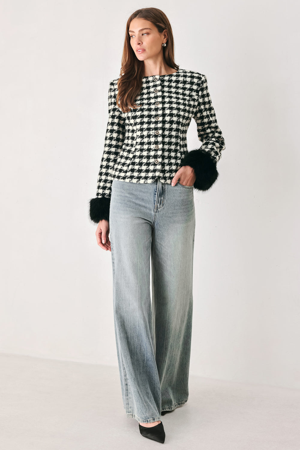 Woman wearing a black and white long sleeve houndstooth tailored jacket with front button closure and faux fur trim around the wrists | FREEMARKET