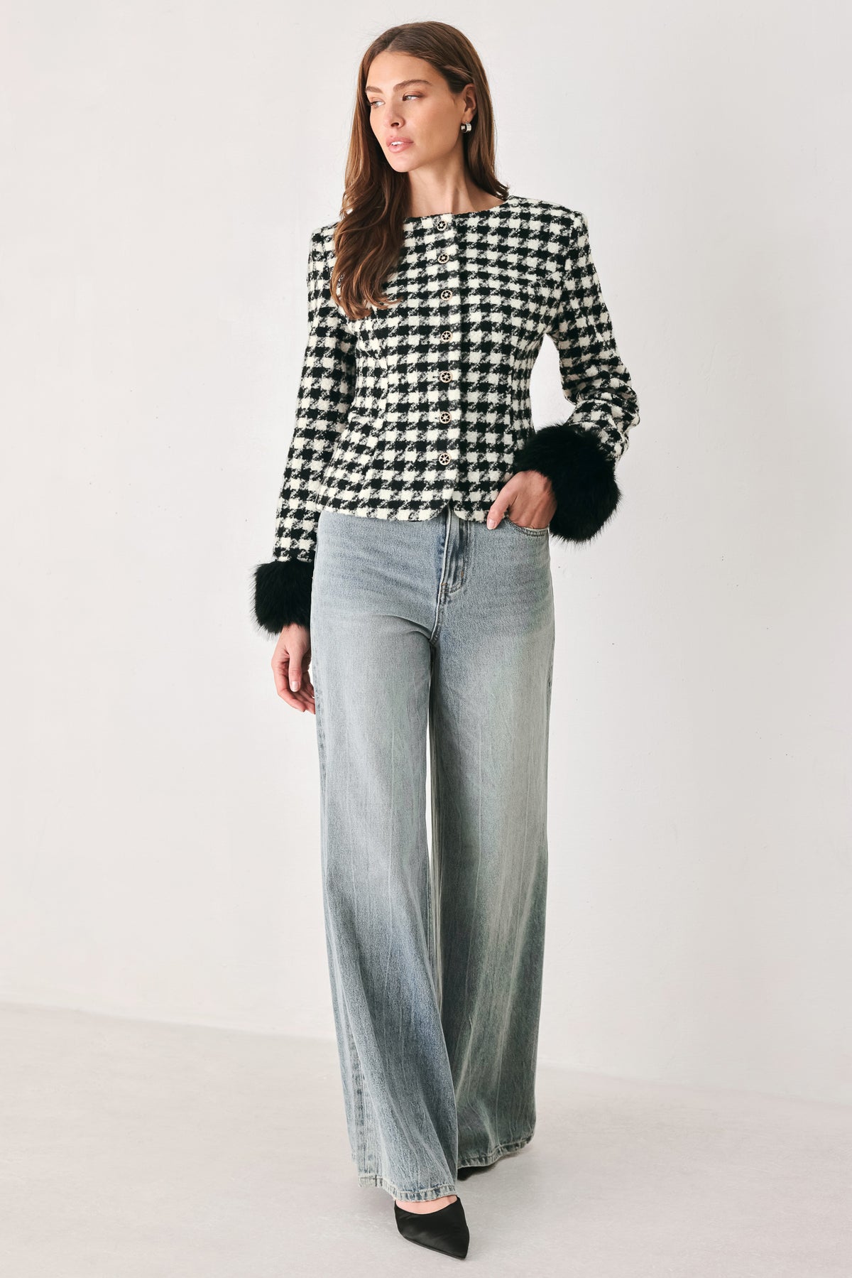 Woman wearing a black and white long sleeve houndstooth tailored jacket with front button closure and faux fur trim around the wrists | FREEMARKET