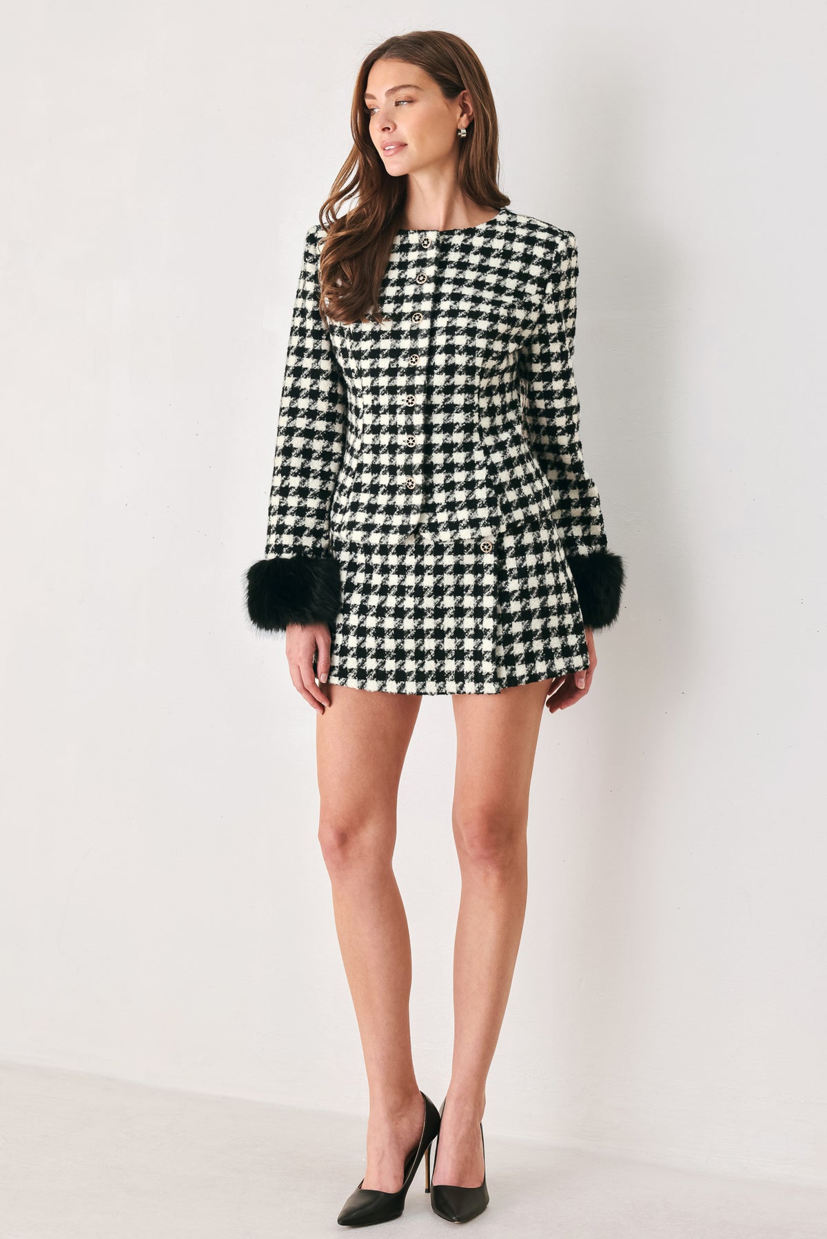 Woman wearing a black and white long sleeve houndstooth tailored jacket with front button closure and faux fur trim around the wrists | FREEMARKET