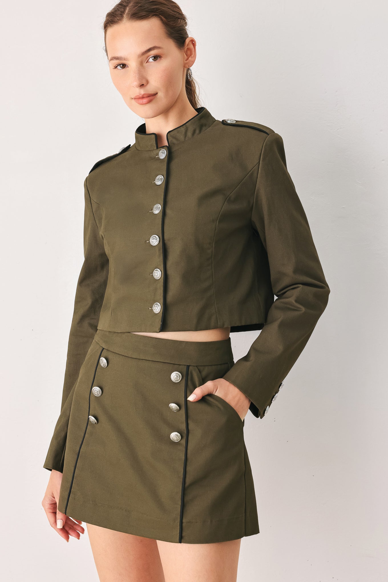 A close-up of a model wearing an olive green cropped jacket with a high stand collar, silver buttons down the front, and shoulder epaulets | FREEMARKET