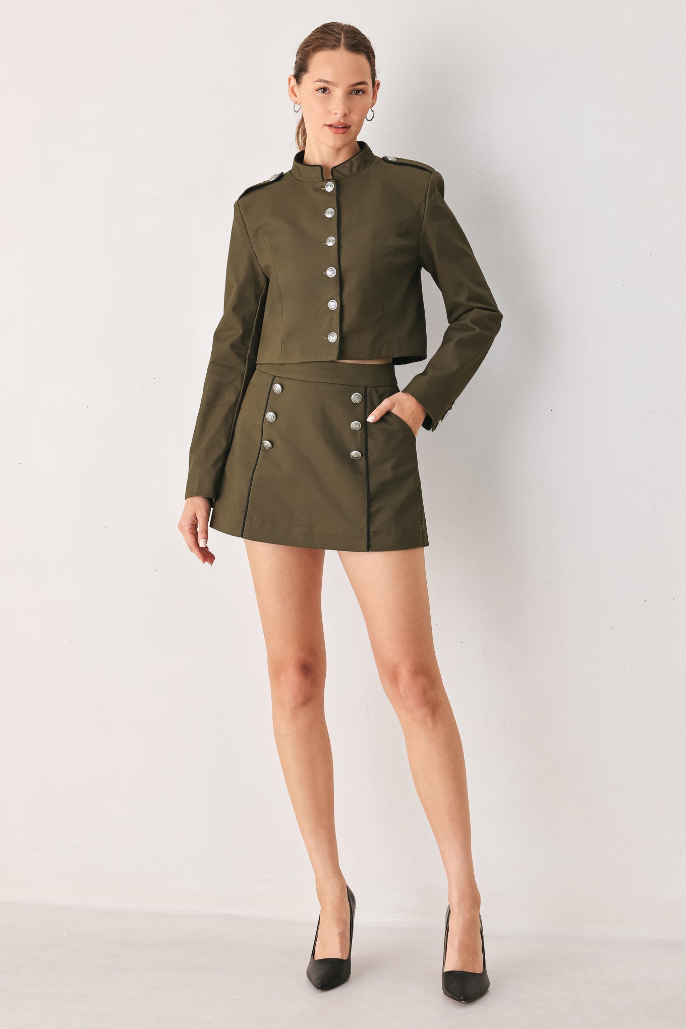 A close-up of a model wearing an olive green cropped jacket with a high stand collar, silver buttons down the front, and shoulder epaulets | FREEMARKET