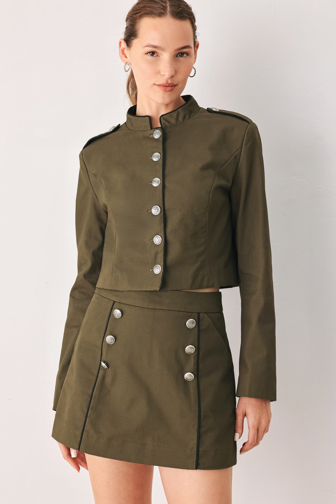 A close-up of a model wearing an olive green cropped jacket with a high stand collar, silver buttons down the front, and shoulder epaulets | FREEMARKET