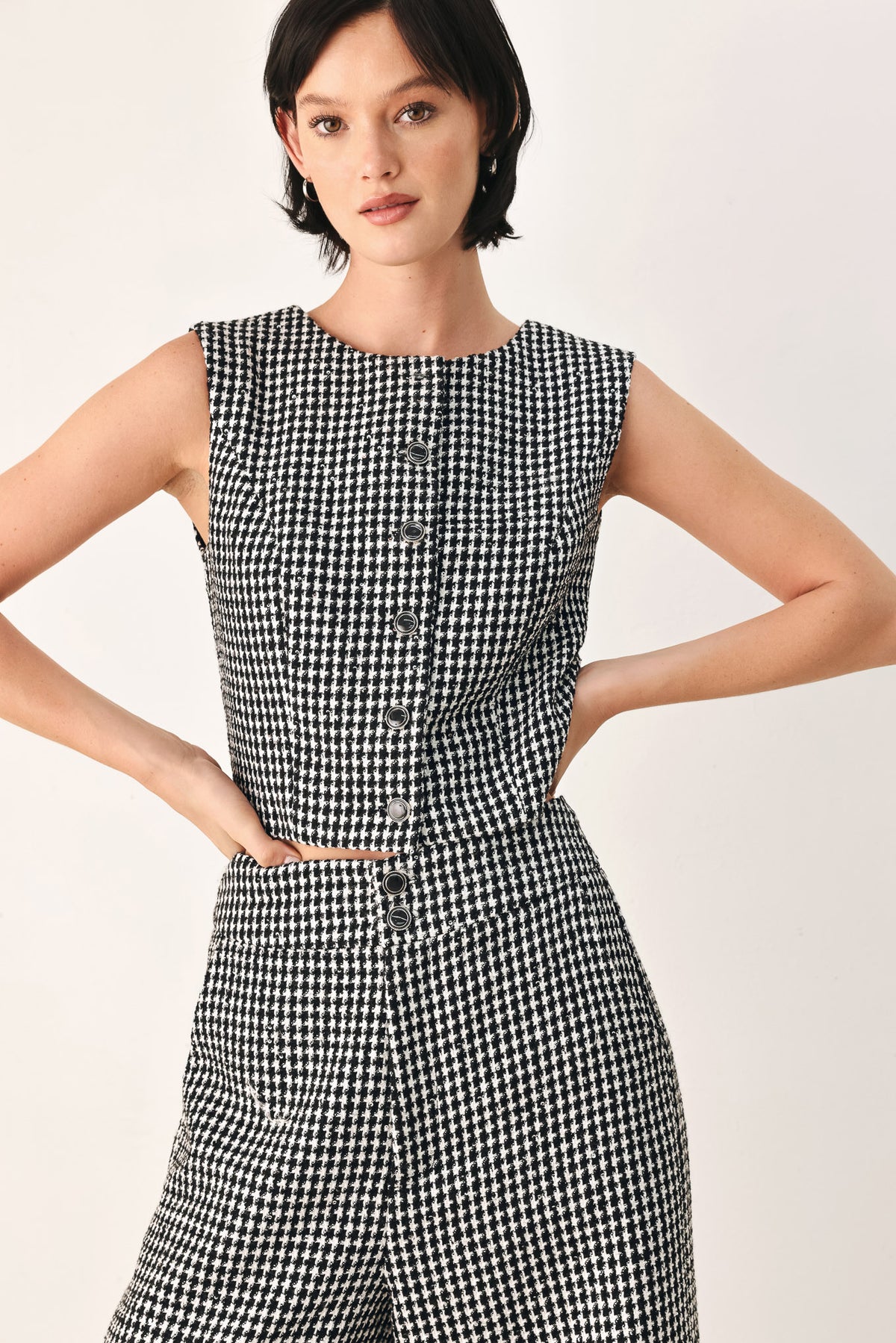 A woman modeling a sleeveless black and white houndstooth cropped vest with a button-front bodice | FREEMARKET