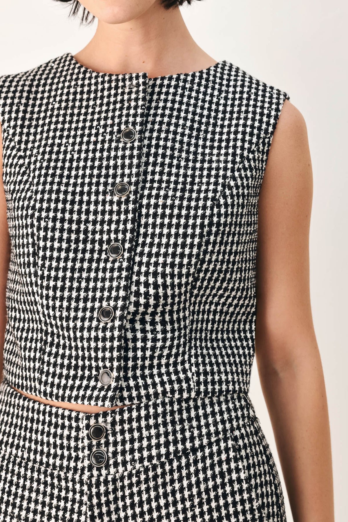 A woman modeling a sleeveless black and white houndstooth cropped vest with a button-front bodice | FREEMARKET