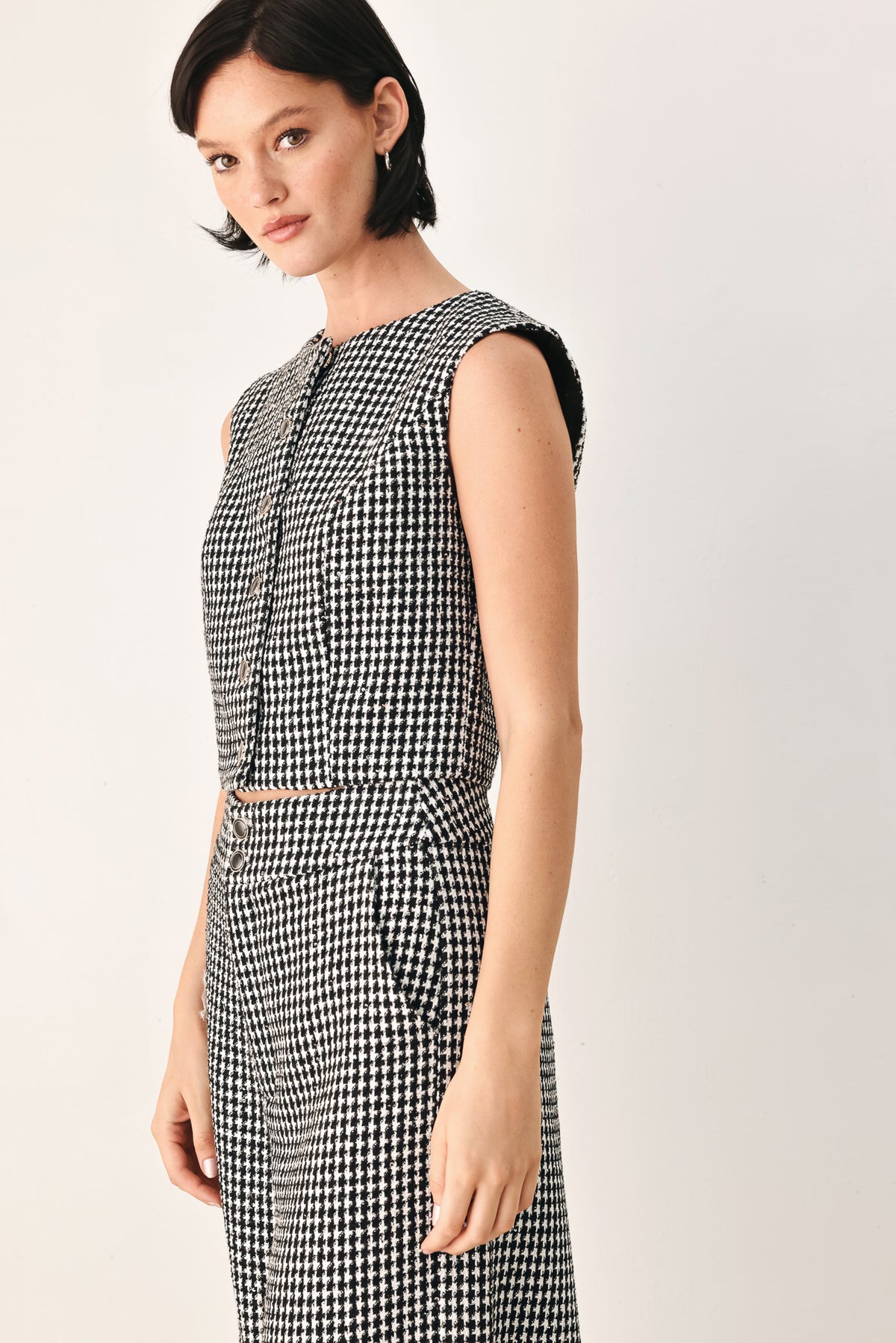 A woman modeling a sleeveless black and white houndstooth cropped vest with a button-front bodice | FREEMARKET