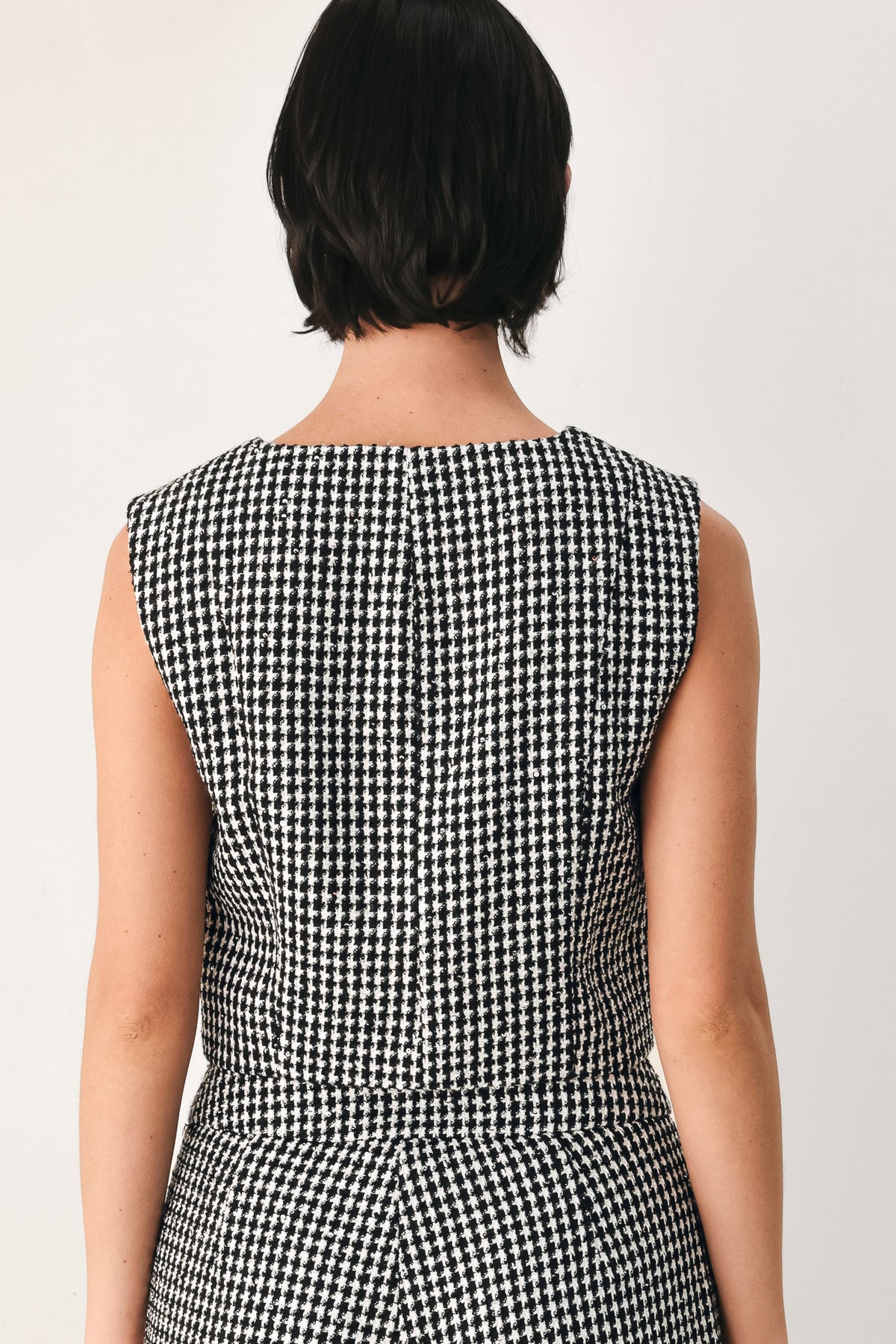 A woman modeling a sleeveless black and white houndstooth cropped vest with a button-front bodice | FREEMARKET