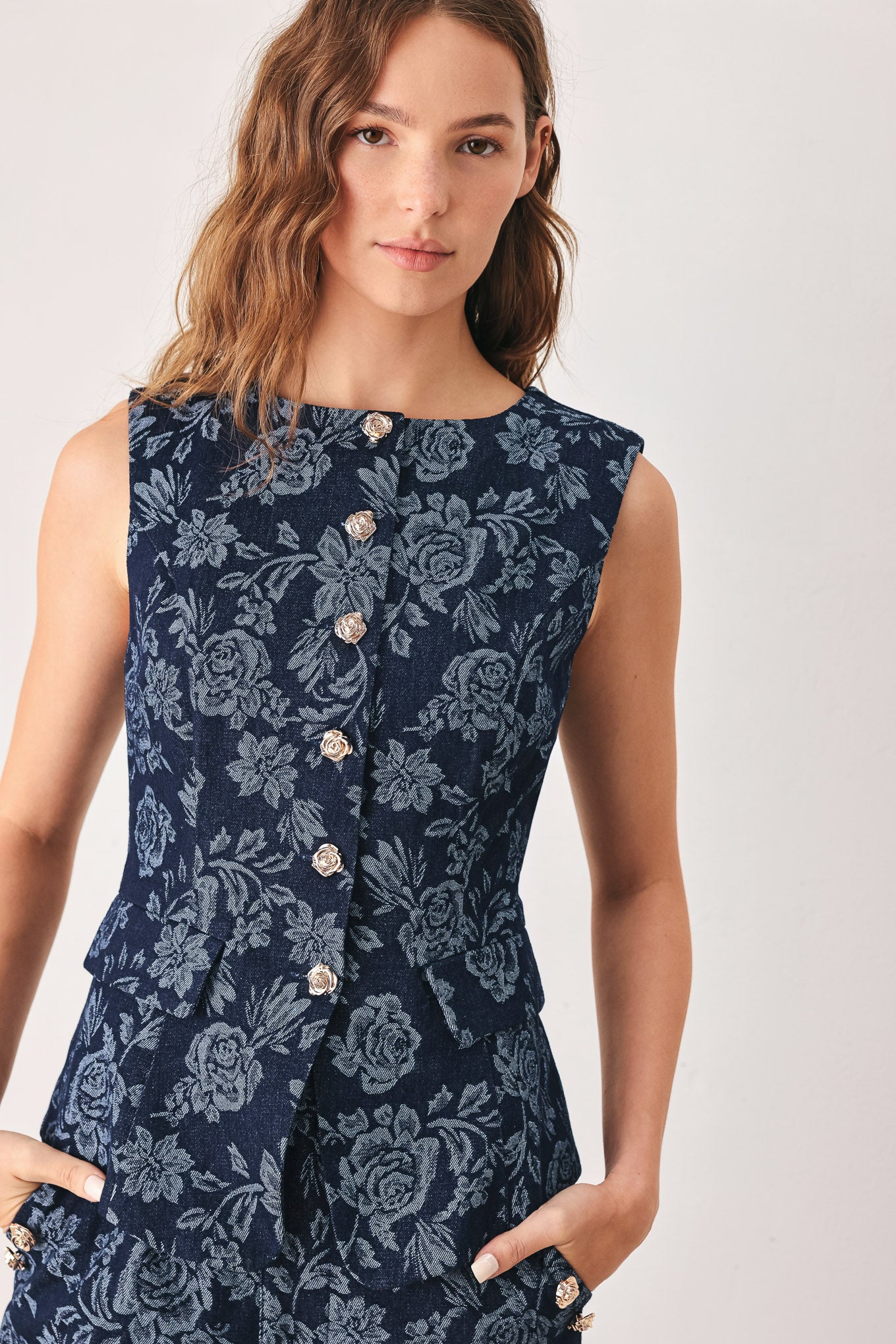 A woman wearing a sleeveless navy blue denim jacquard vest with a light blue floral pattern and gold-tone buttons down the front | FREEMARKET