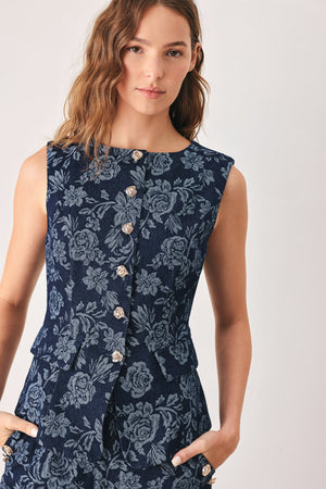 A woman wearing a sleeveless navy blue denim jacquard vest with a light blue floral pattern and gold-tone buttons down the front | FREEMARKET