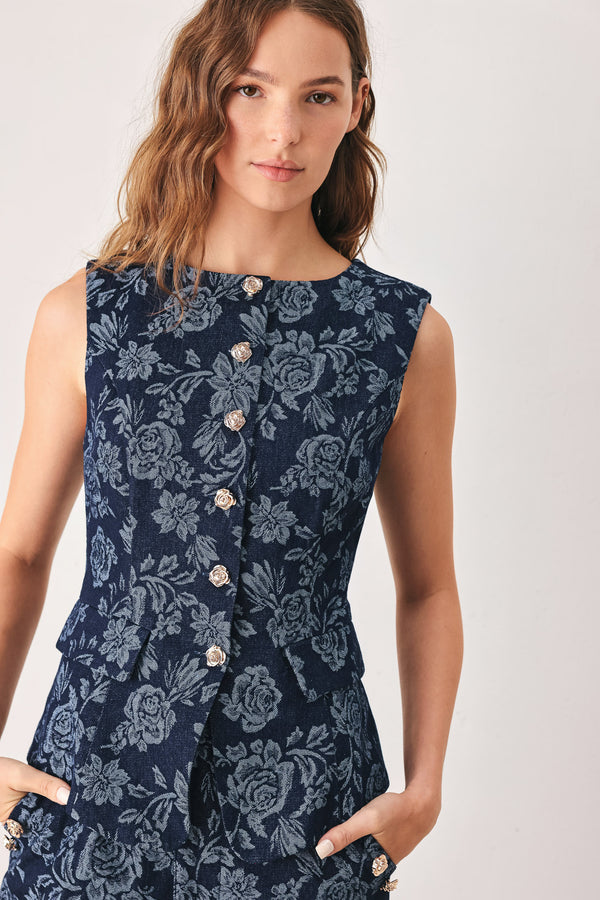A woman wearing a sleeveless navy blue denim jacquard vest with a light blue floral pattern and gold-tone buttons down the front | FREEMARKET