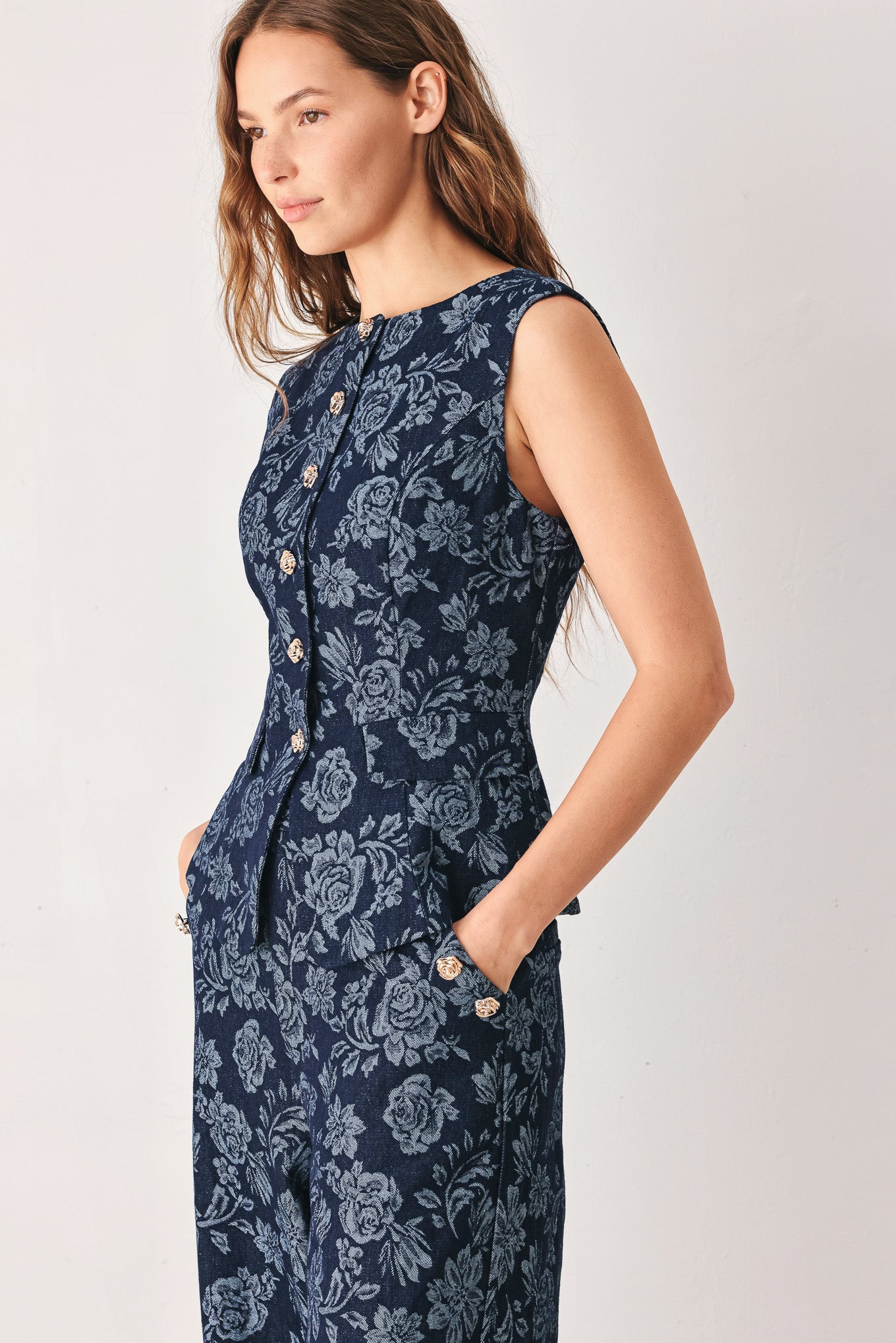 A woman wearing a sleeveless navy blue denim jacquard vest with a light blue floral pattern and gold-tone buttons down the front | FREEMARKET