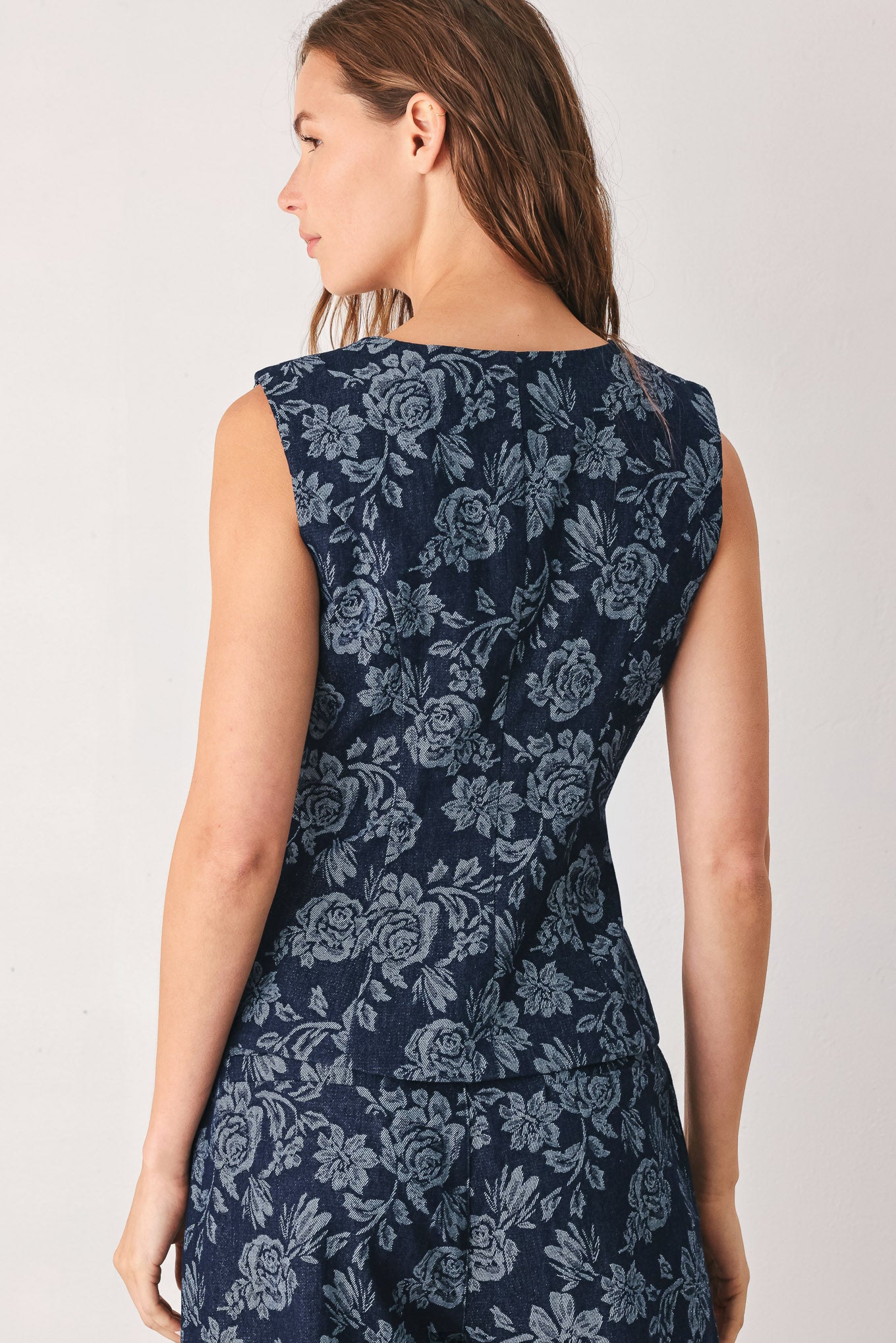 A woman wearing a sleeveless navy blue denim jacquard vest with a light blue floral pattern and gold-tone buttons down the front | FREEMARKET