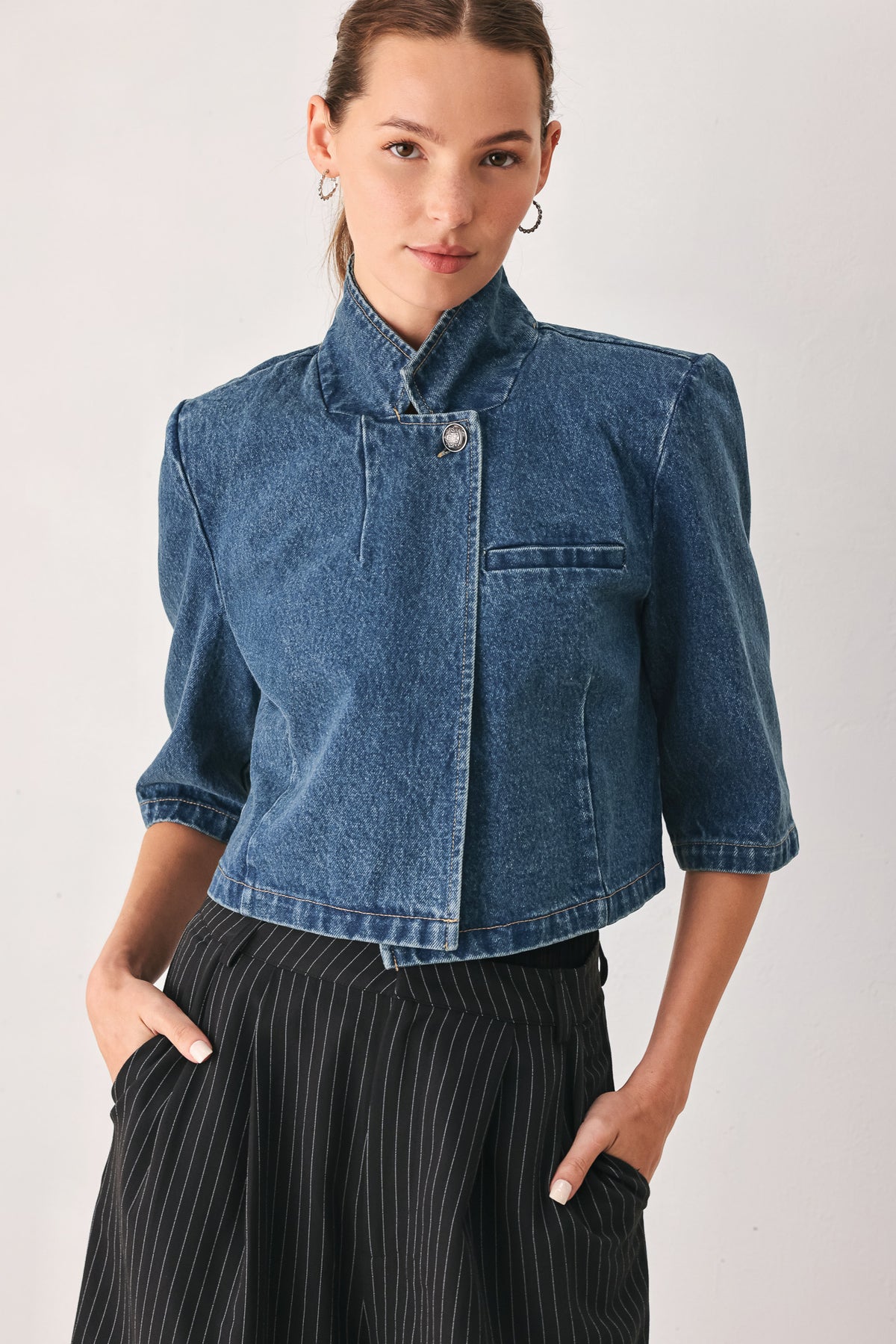 A woman wearing a cropped blue denim jacket with a high stand collar, structured shoulders, and elbow-length sleeves | FREEMARKET