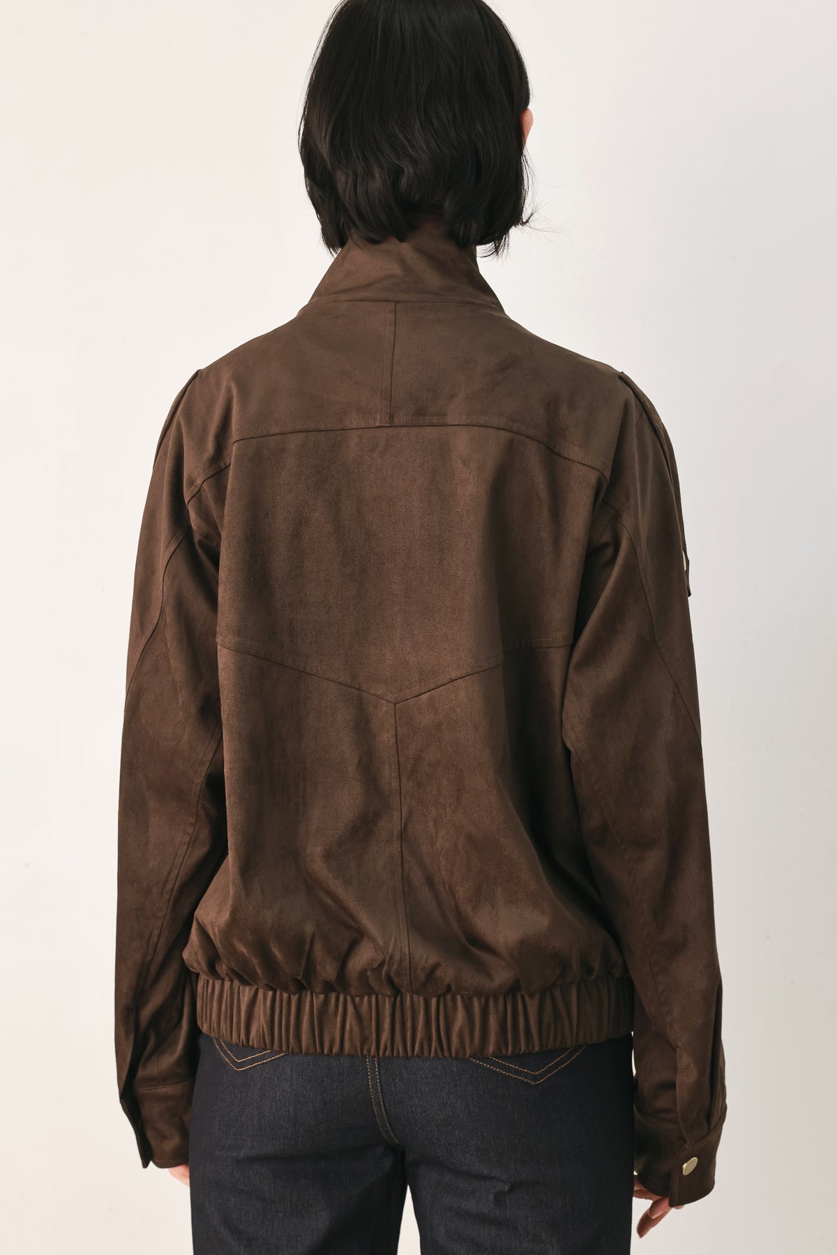A woman wearing a dark brown suede jacket with a high collar and gold-tone snap buttons | FREEMARKET