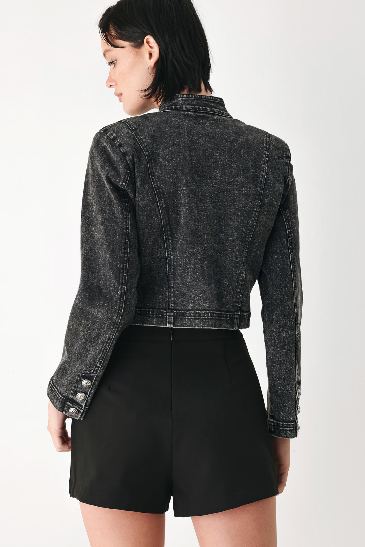 A model wearing a cropped black washed denim jacket with silver-tone decorative buttons | FREEMARKET