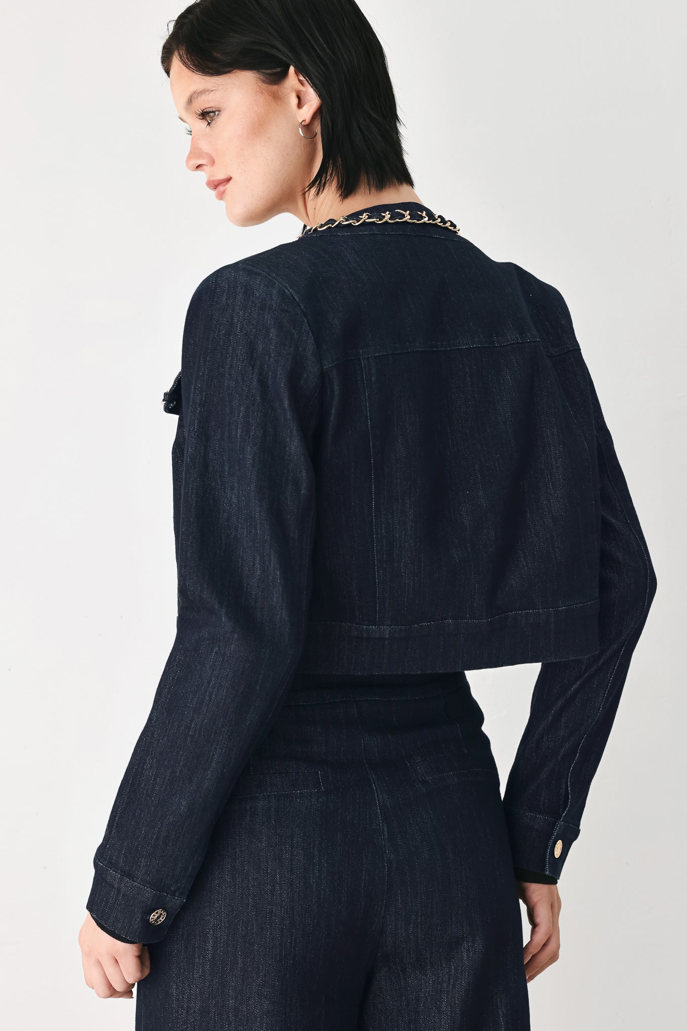 A model wearing a dark indigo denim jacket featuring gold chain trim details on the collar, chest pockets | FREEMARKET