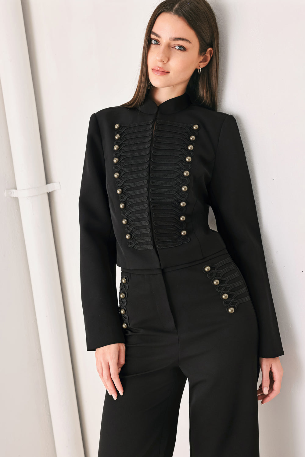 Woman wearing a long-sleeve mock neck black cropped jacket top with double breasted buttons and military style braiding | FREEMARKET