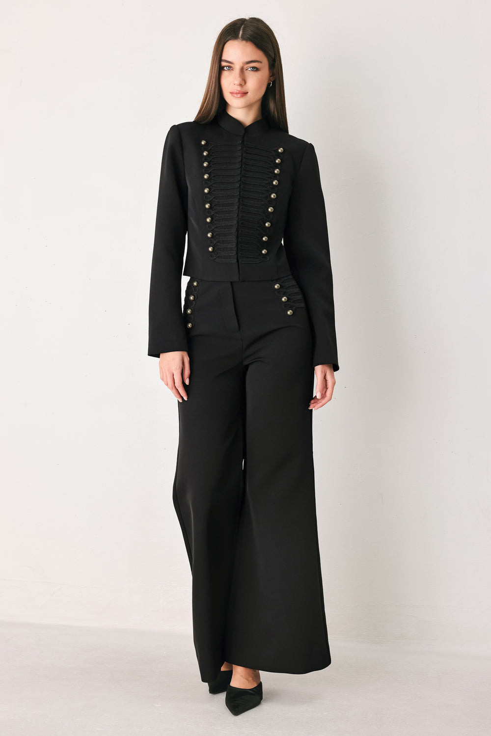 Woman wearing a long-sleeve mock neck black cropped jacket top with double breasted buttons and military style braiding | FREEMARKET