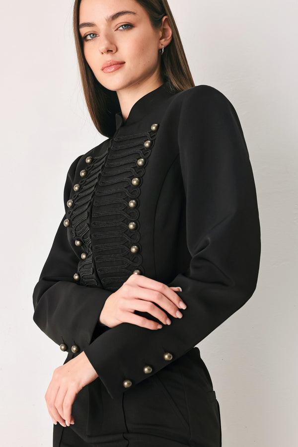 Woman wearing a long-sleeve mock neck black cropped jacket top with double breasted buttons and military style braiding | FREEMARKET