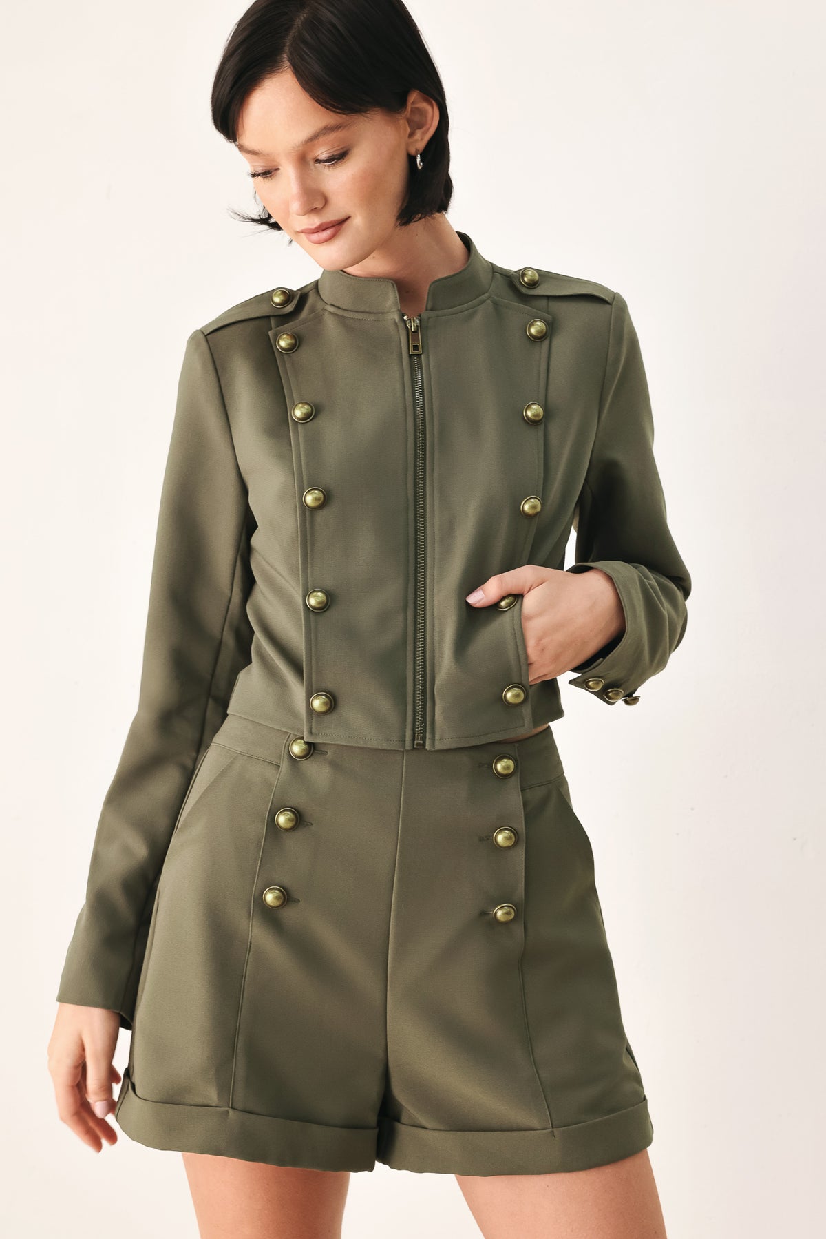 A model wearing an olive green military-style cropped jacket top with gold-tone double-breasted buttons, a front zipper, and a high mock neck | FREEMARKET