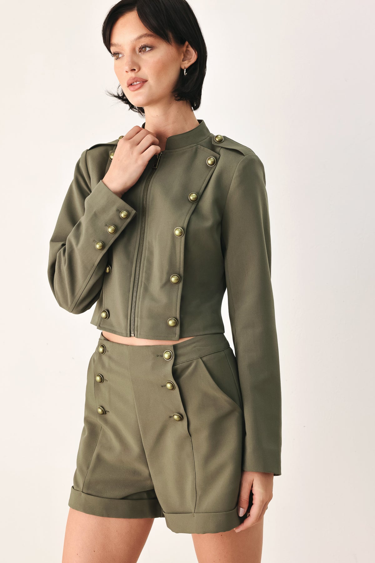 A model wearing an olive green military-style cropped jacket top with gold-tone double-breasted buttons, a front zipper, and a high mock neck | FREEMARKET