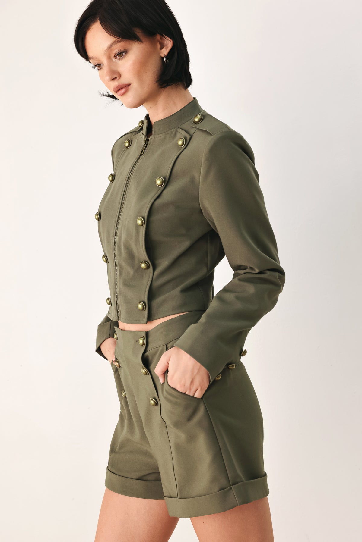 A model wearing an olive green military-style cropped jacket top with gold-tone double-breasted buttons, a front zipper, and a high mock neck | FREEMARKET