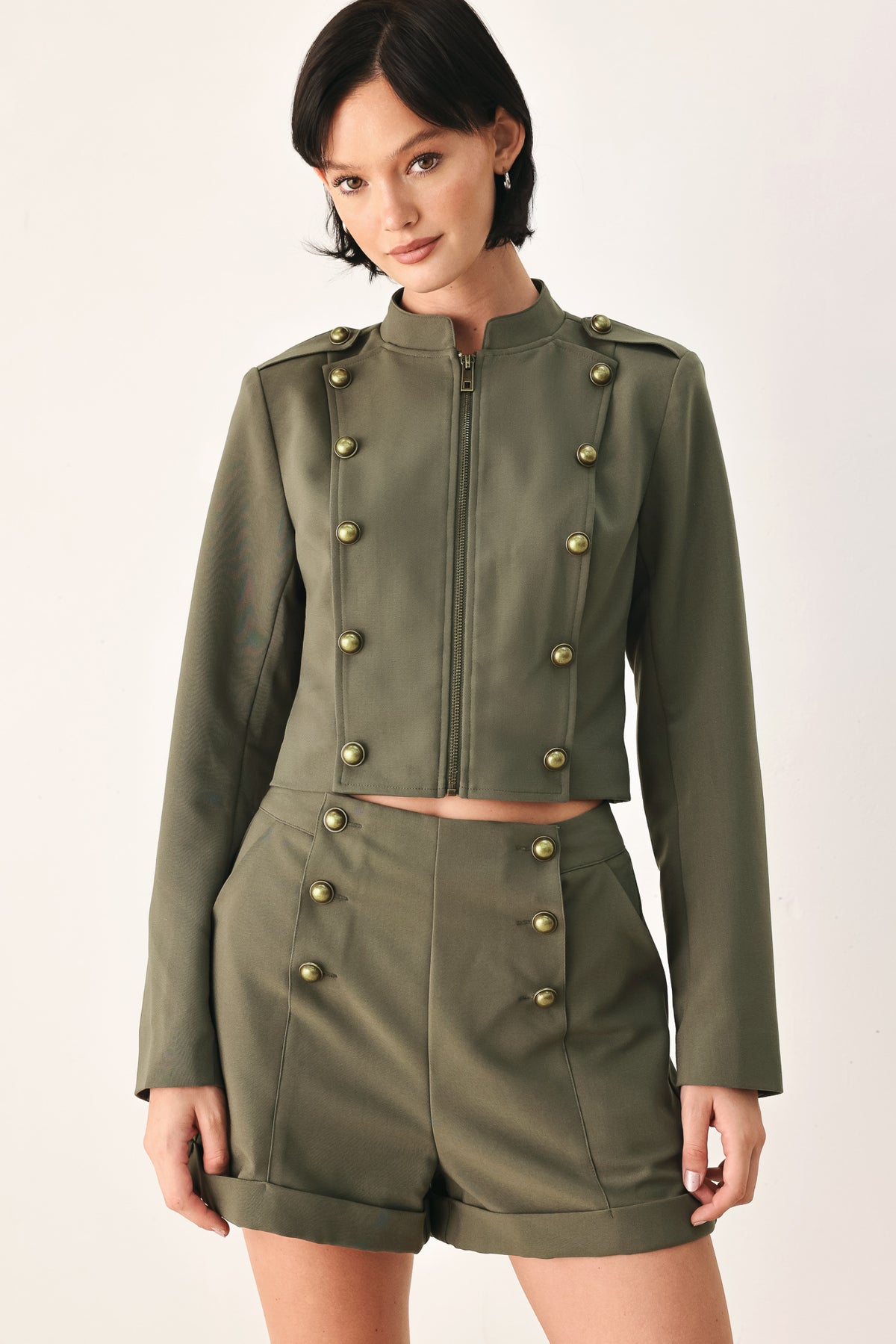 A model wearing an olive green military-style cropped jacket top with gold-tone double-breasted buttons, a front zipper, and a high mock neck | FREEMARKET