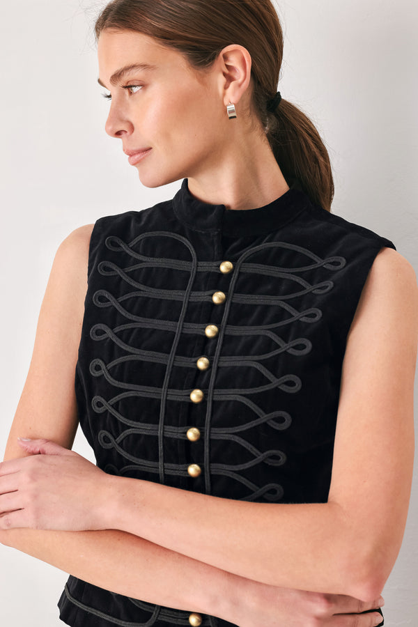 A sleeveless black top with a high mock neck, featuring a central row of gold buttons and dark gray decorative cord-like embroidery across the front, shown on a model.