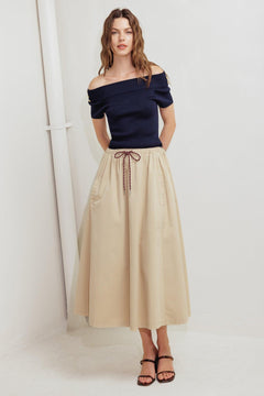 A solid woven midi skirt featuring elasticized waistband with contrasting front tie, side pockets and full skirt