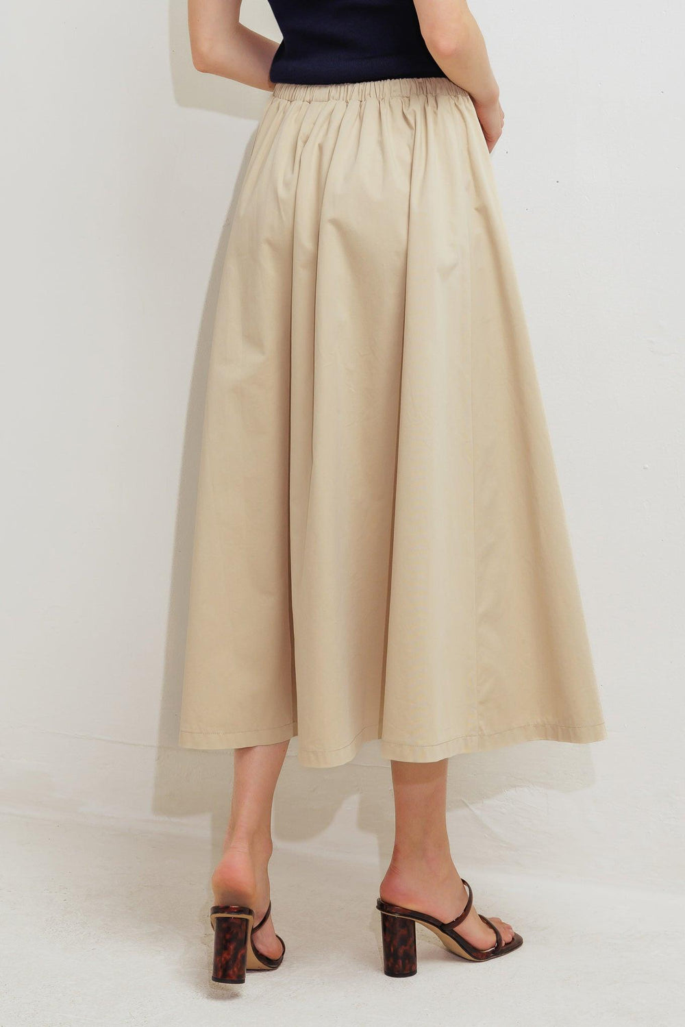A solid woven midi skirt featuring elasticized waistband with contrasting front tie, side pockets and full skirt