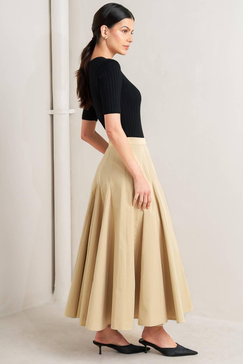 Woman wearing a black top and beige skirt against a neutral background - FLYING TOMATO