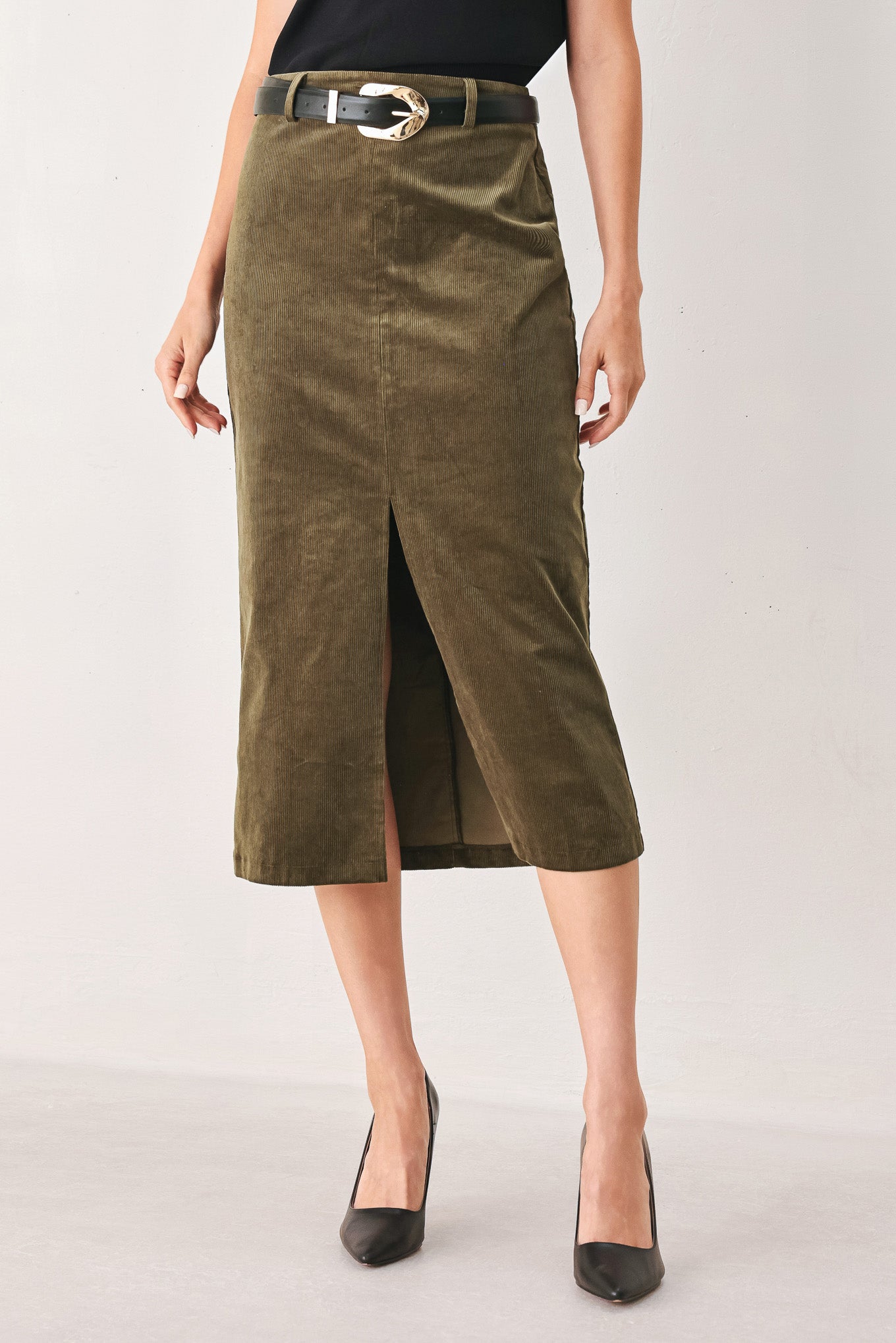 A woman wearing an olive green corduroy midi skirt with a front slit, styled with a black belt featuring a silver buckle | FREEMARKET