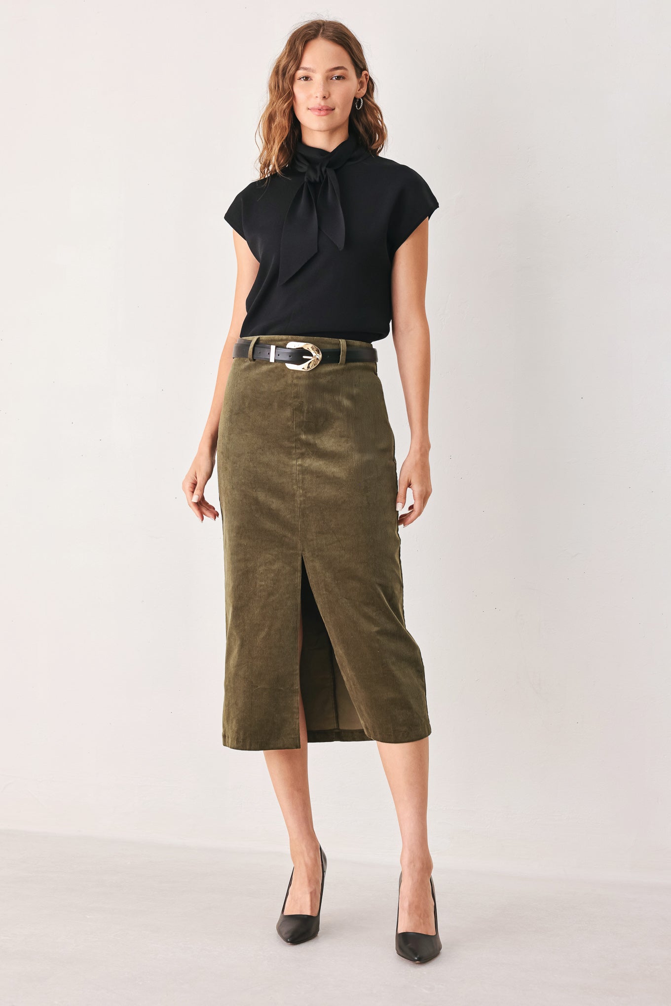 A woman wearing an olive green corduroy midi skirt with a front slit, styled with a black belt featuring a silver buckle | FREEMARKET