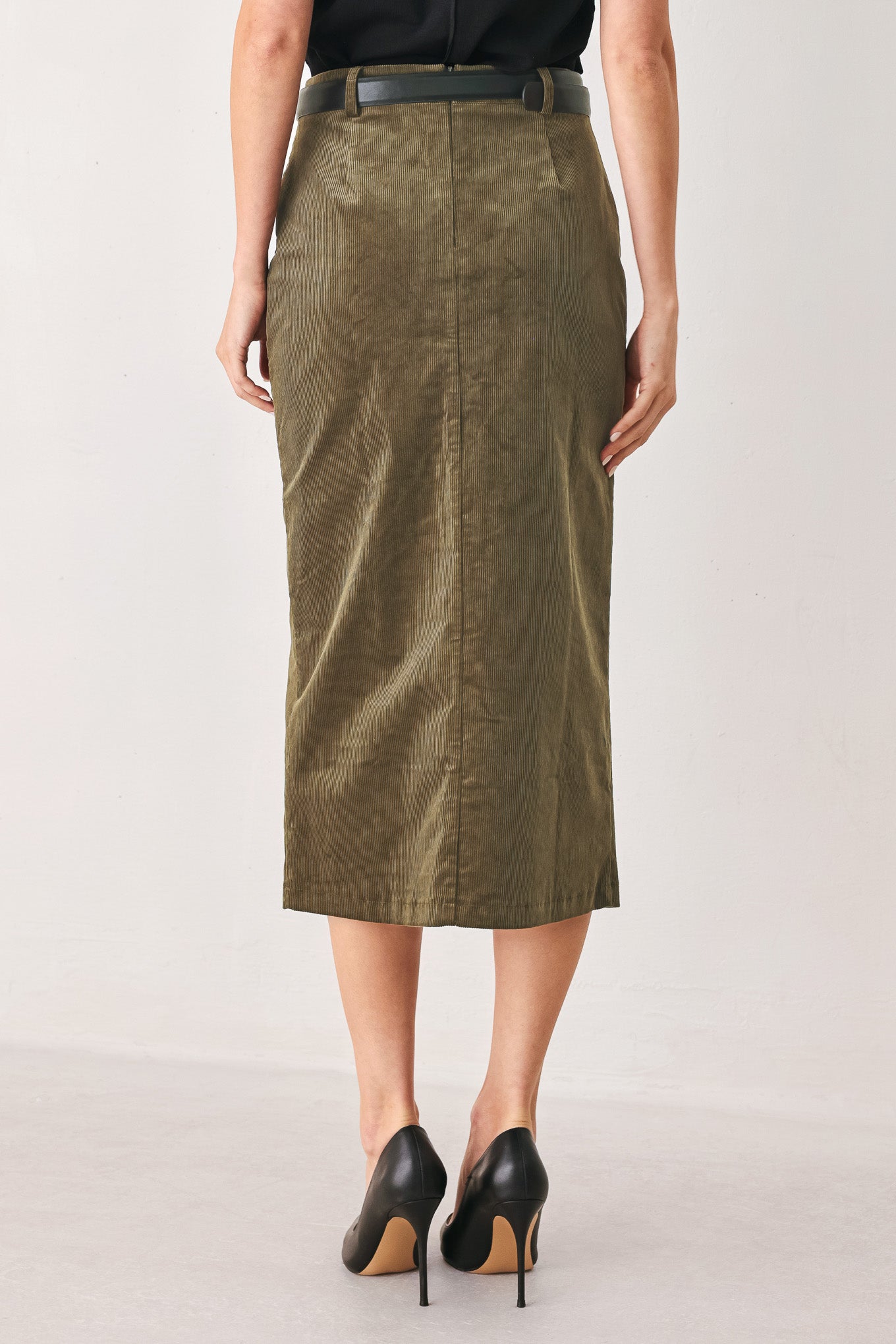 A woman wearing an olive green corduroy midi skirt with a front slit, styled with a black belt featuring a silver buckle | FREEMARKET