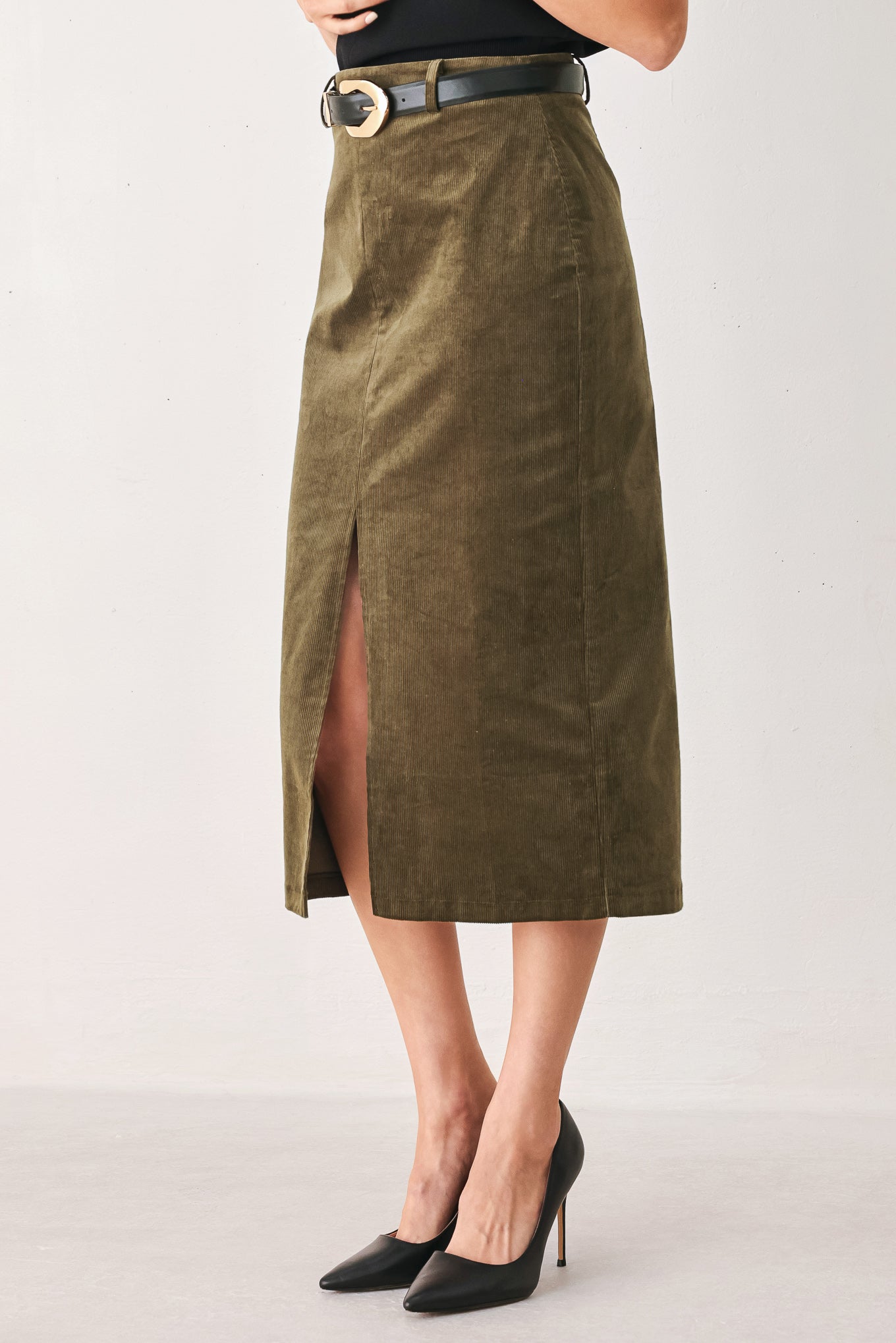 A woman wearing an olive green corduroy midi skirt with a front slit, styled with a black belt featuring a silver buckle | FREEMARKET