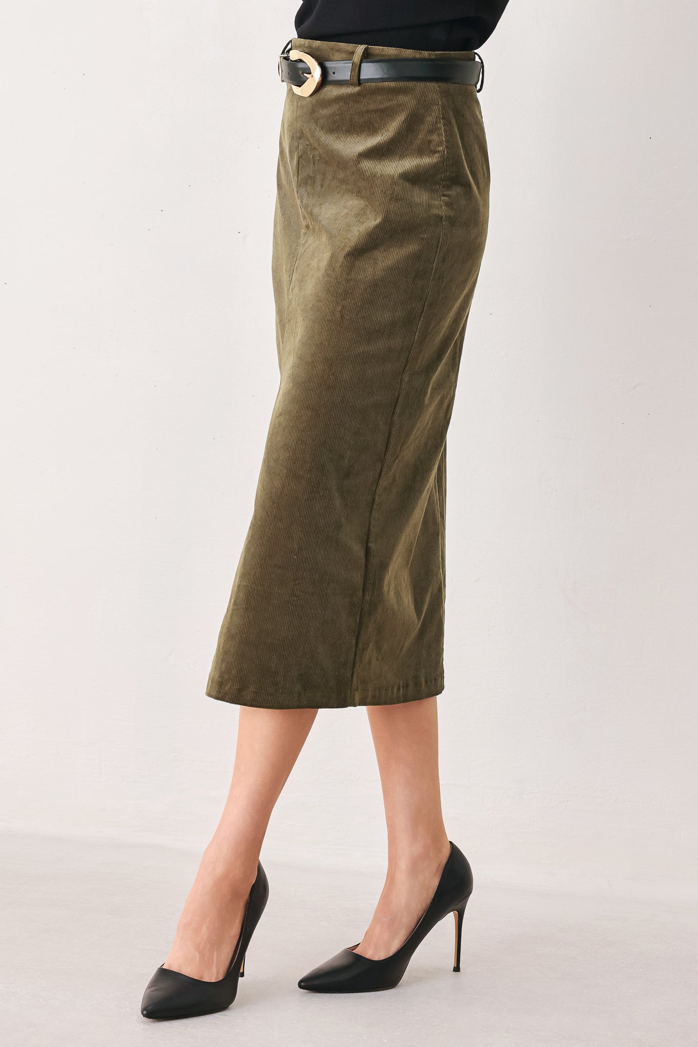 A woman wearing an olive green corduroy midi skirt with a front slit, styled with a black belt featuring a silver buckle | FREEMARKET