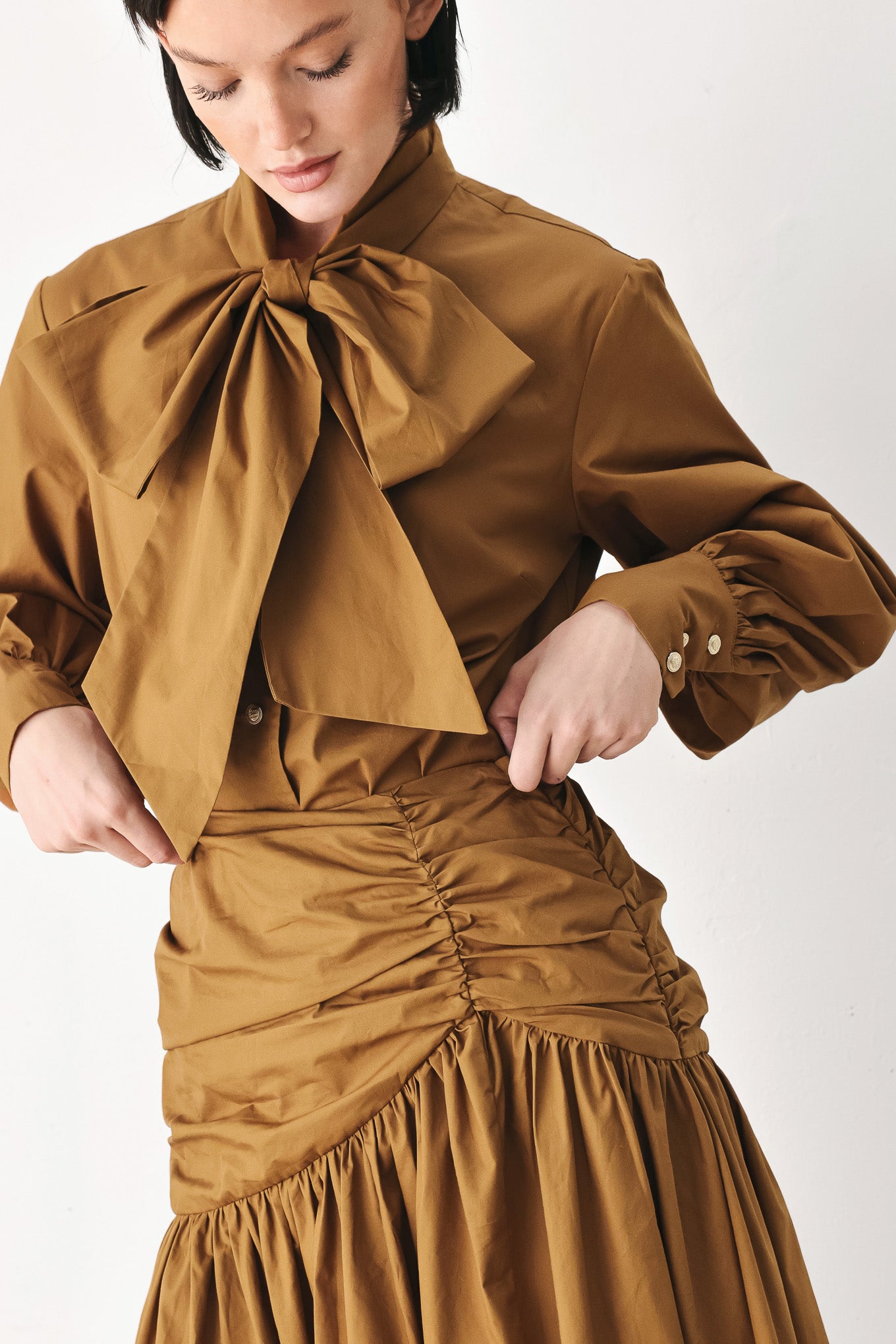 A model wearing a high-waisted, ruched A-line midi skirt in a warm caramel brown color | FREEMARKET