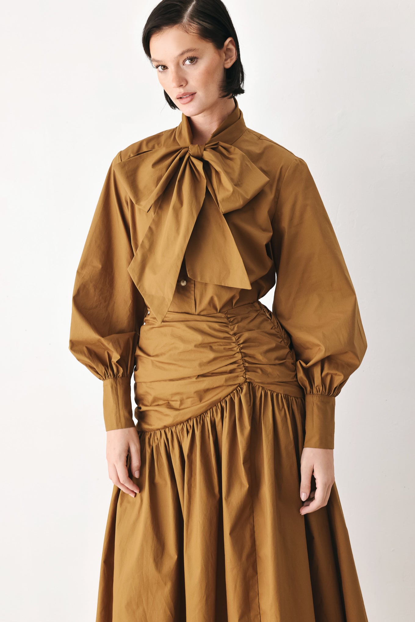 A model wearing a high-waisted, ruched A-line midi skirt in a warm caramel brown color | FREEMARKET