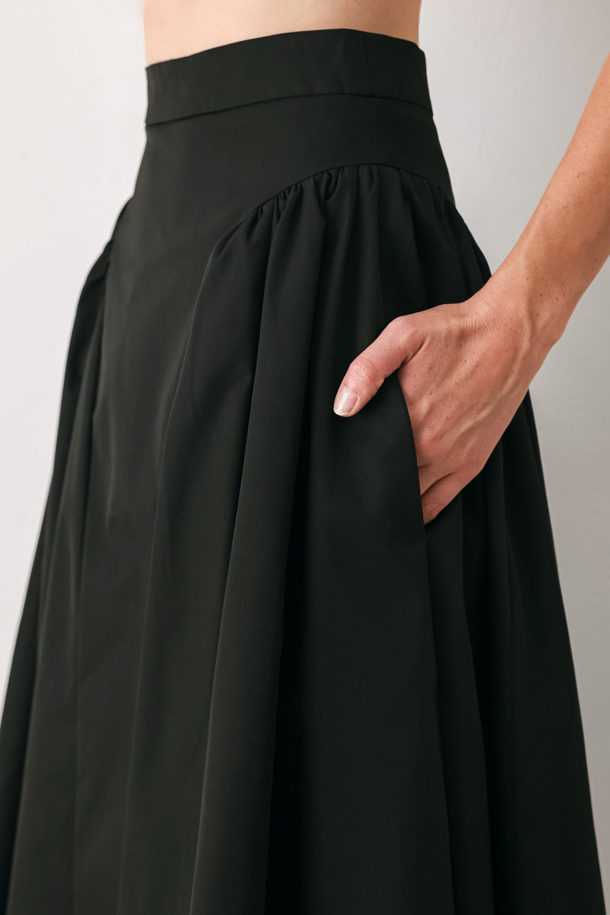 Woman wearing a high waisted black midi skirt with side shirring along the hips | FREEMARKET