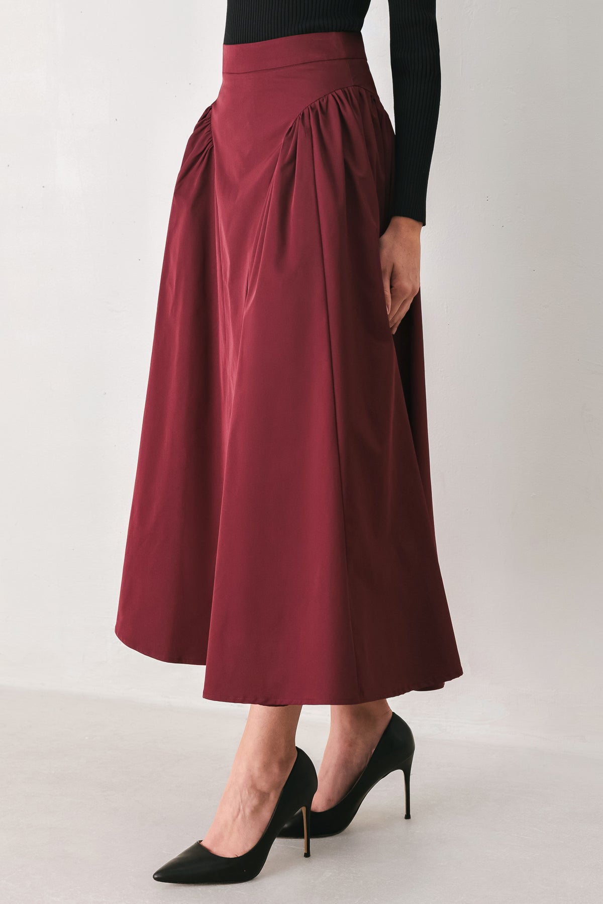 Woman wearing a high waisted burgundy midi skirt with side shirring along the hips | FREEMARKET
