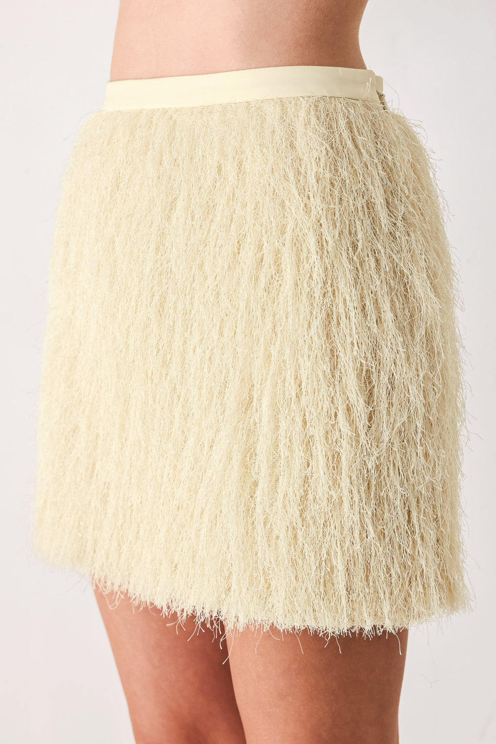 A close-up of a model wearing a cream-colored, shaggy, textured mini skirt | FREEMARKET