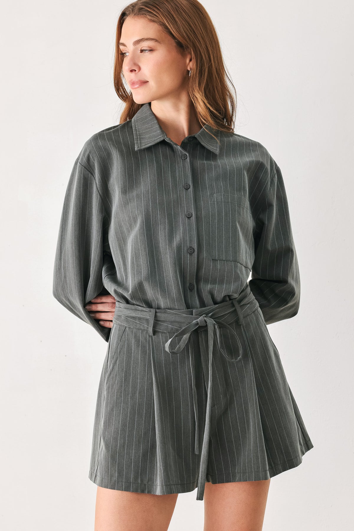 A woman modeling a dark gray pinstriped long-sleeve shirt dress with a tie waist belt | FREEMARKET 