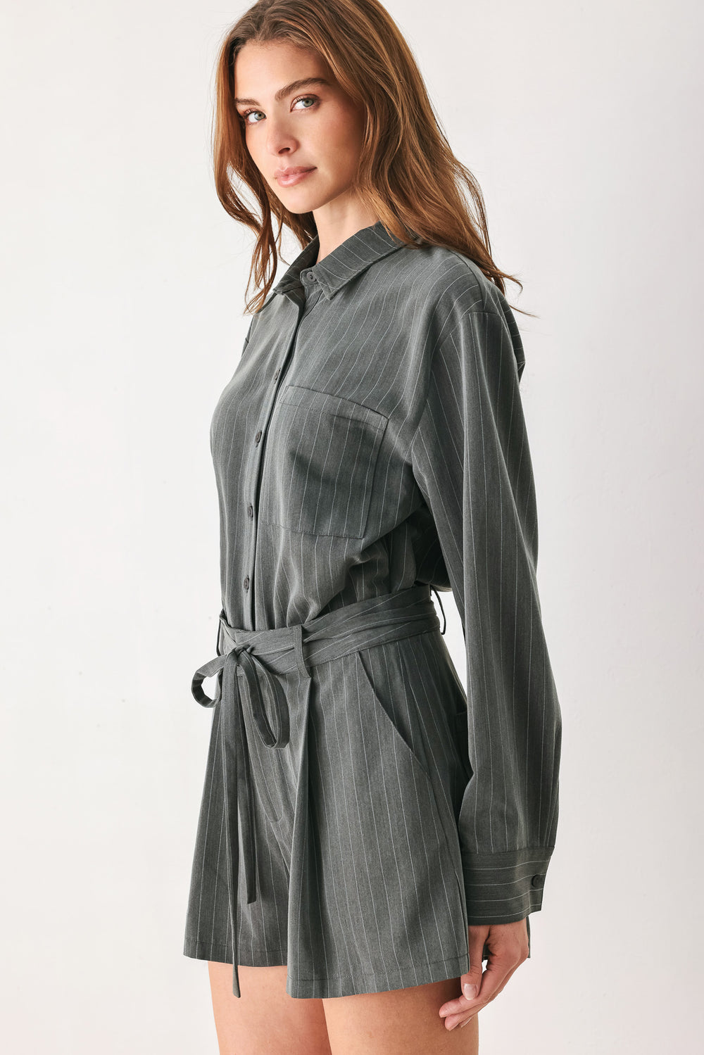 A woman modeling a dark gray pinstriped long-sleeve shirt dress with a tie waist belt | FREEMARKET 