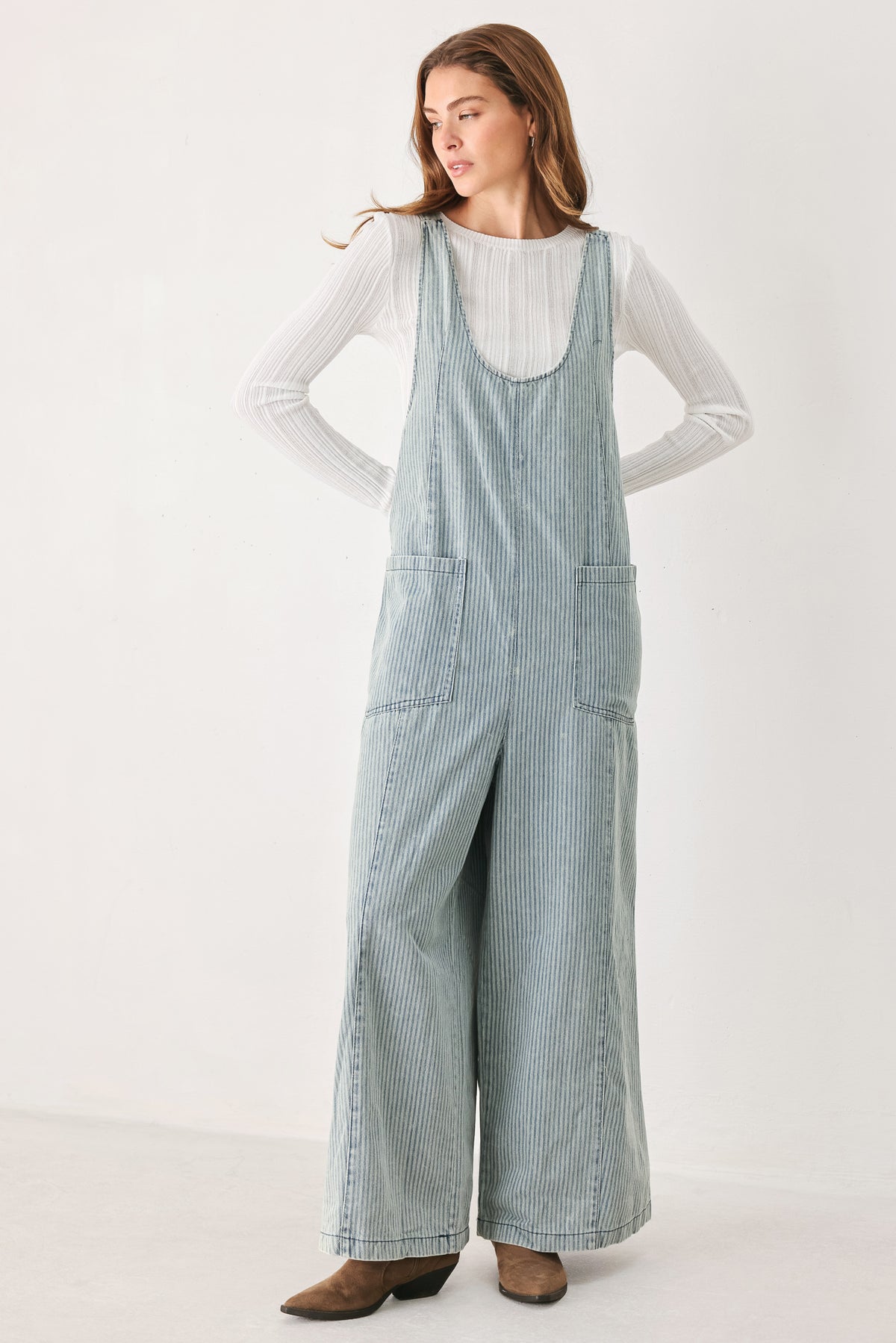 A woman wearing a light blue and white vertically striped corduroy bib jumpsuit over a white long-sleeve top | FREEMARKET