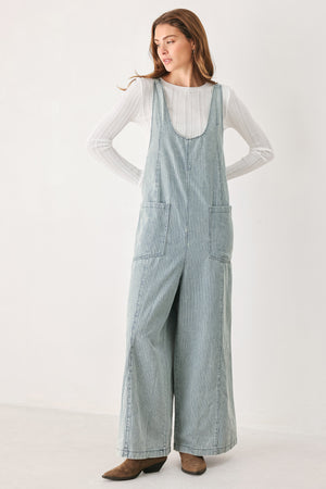 A woman wearing a light blue and white vertically striped corduroy bib jumpsuit over a white long-sleeve top | FREEMARKET