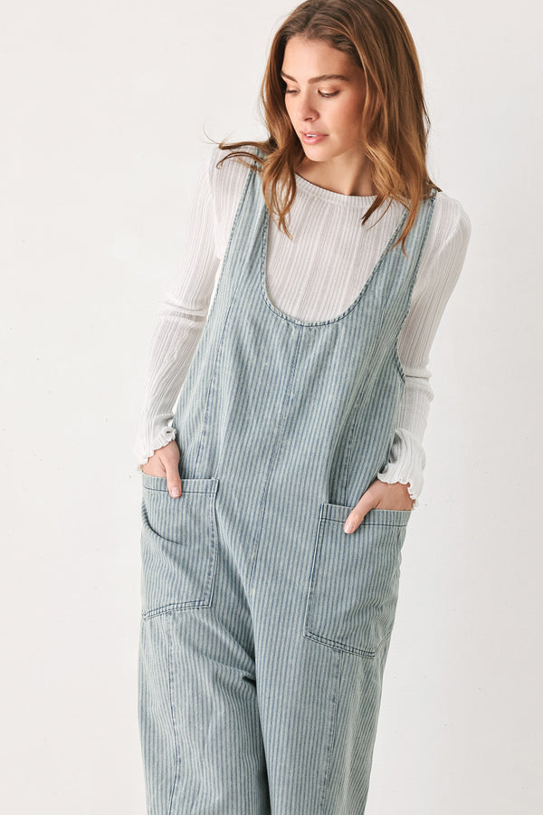 A woman wearing a light blue and white vertically striped corduroy bib jumpsuit over a white long-sleeve top | FREEMARKET