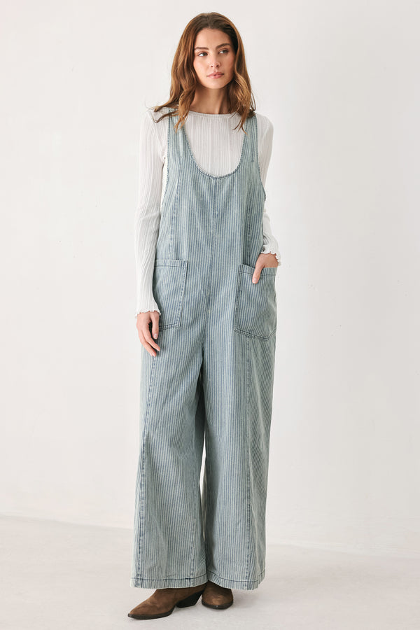 A woman wearing a light blue and white vertically striped corduroy bib jumpsuit over a white long-sleeve top | FREEMARKET