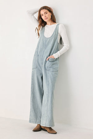 A woman wearing a light blue and white vertically striped corduroy bib jumpsuit over a white long-sleeve top | FREEMARKET